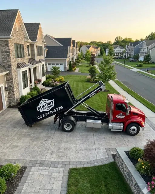 Summit Carting roll-off truck delivering a black Summit dumpster on a paver driveway in a Connecticut neighborhood