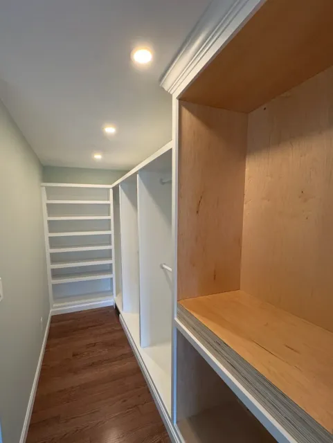 Cypress Works Massachusetts, a custom walk-in closet with built-in white shelves and hanging rods, featuring wooden flooring and recessed ceiling lights.
