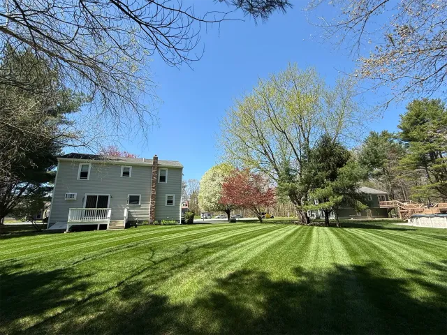 Lawn with freshly cut stripes, a two-story house, trees, and a clear blue sky.
