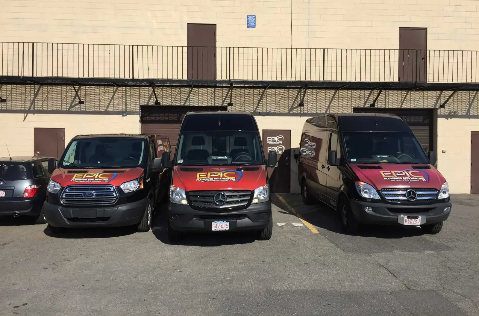 Three vans with company logos parked in front of a building. Sunny day.