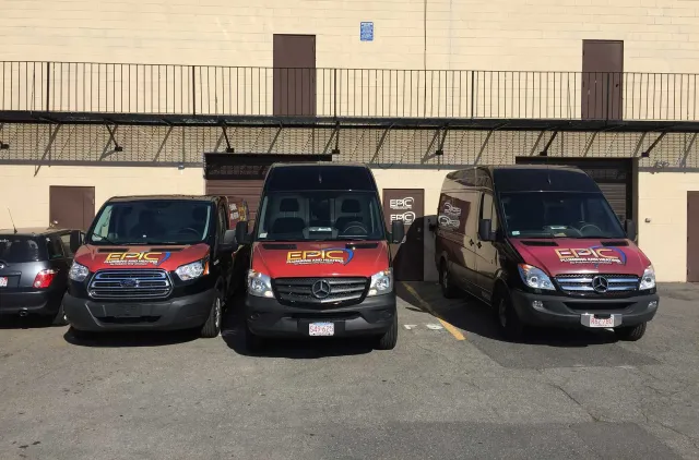 Three vans with company logos parked in front of a building. Sunny day.