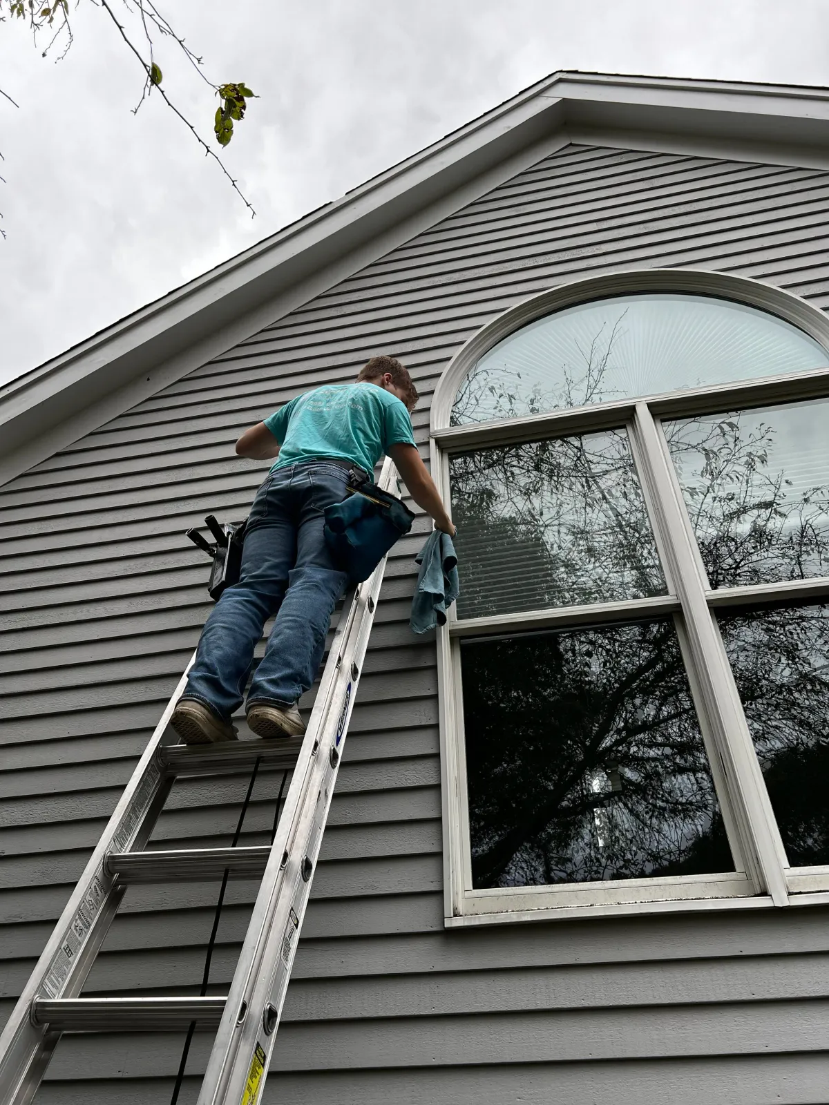 Person cleaning arched window on ladder