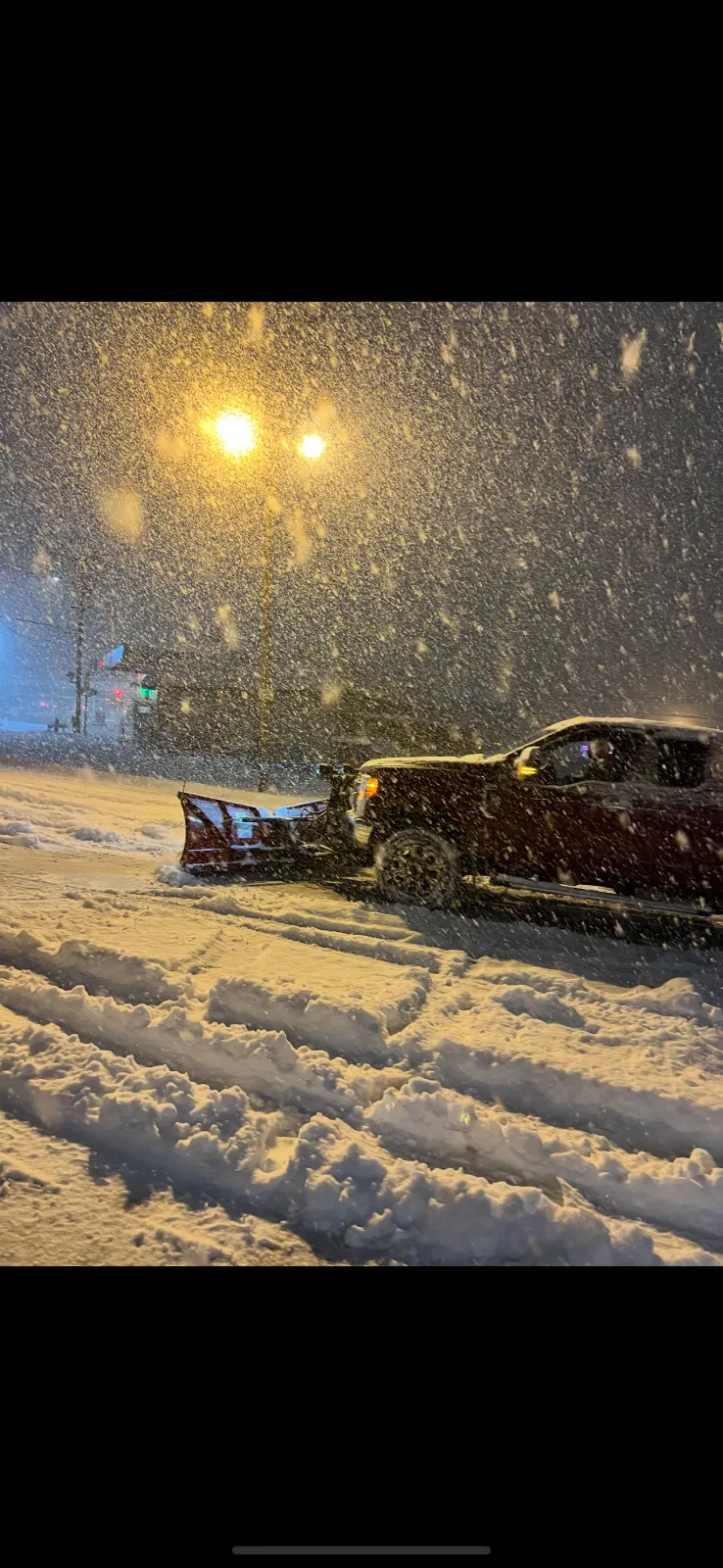 A snow plow is clearing snow from a parking lot at night.