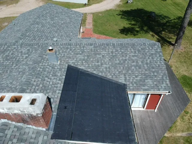 Aerial view of a house roof with gray shingles, a black skylight, and a red door visible at the side.