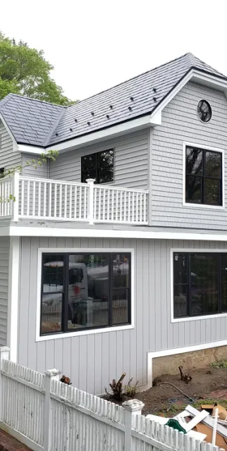 Modern gray two-story house renovation featuring white siding, a rooftop deck, and new black frame windows.