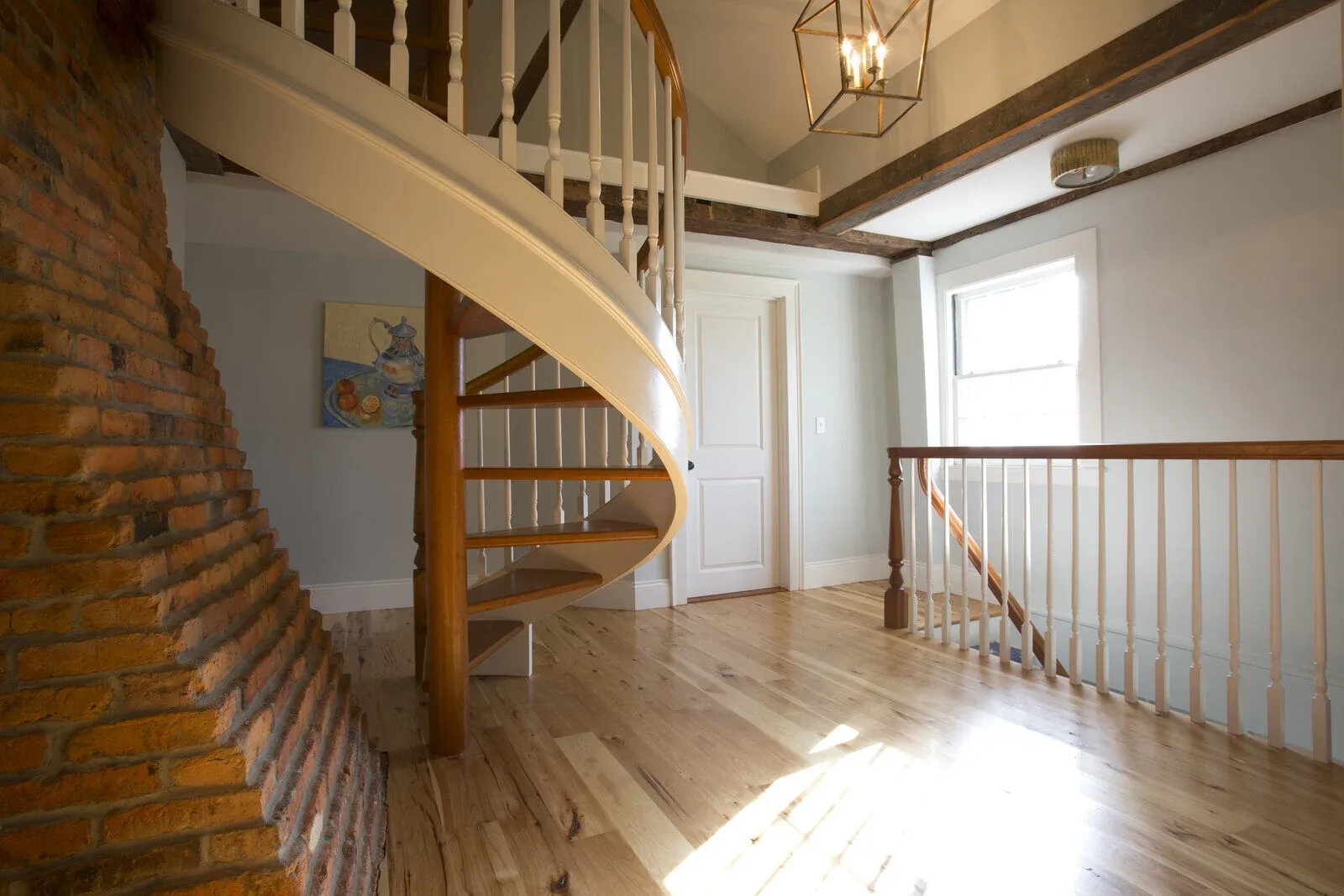 Loft area with a wooden spiral staircase and exposed brick wall, a unique design by Oxland Builders in New Hampshire