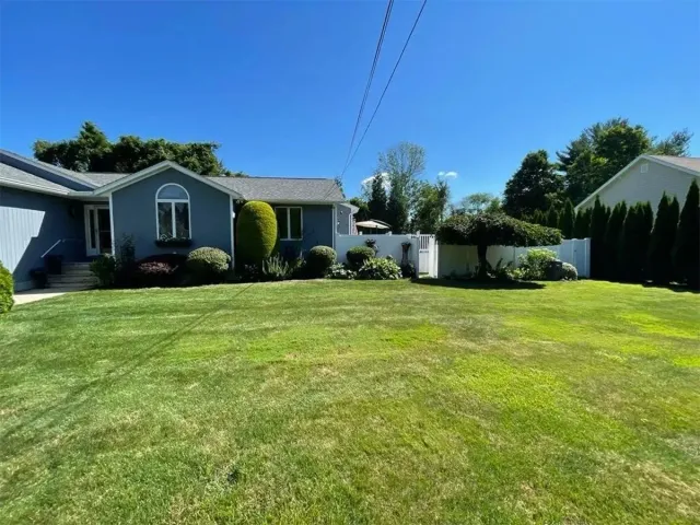 Suburban house with a large green lawn, shrubs, and a clear blue sky.