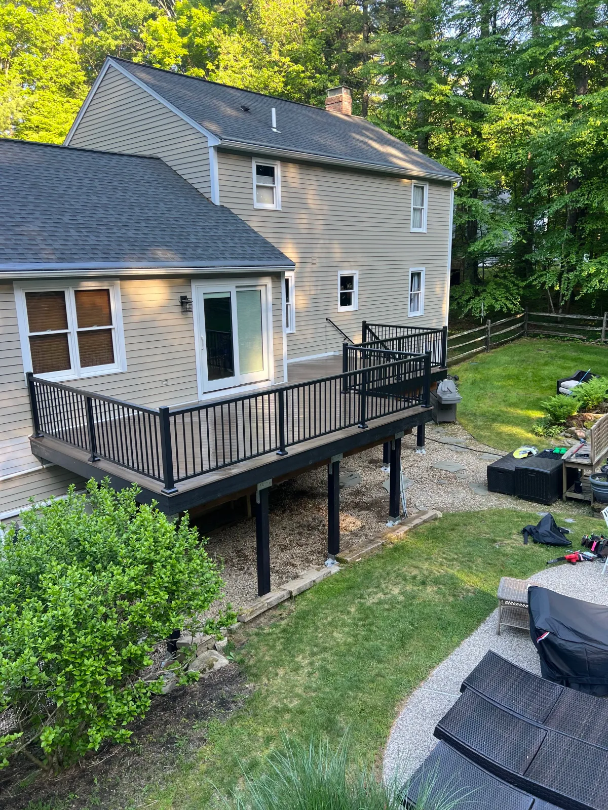 A newly built raised deck attached to a light yellow house with steps leading down to a grassy yard.