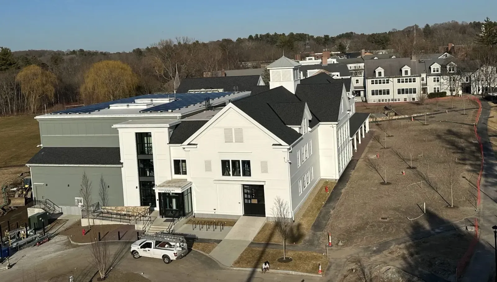 White building with dark roof, solar panels, and unfinished construction area on a sunny day.
