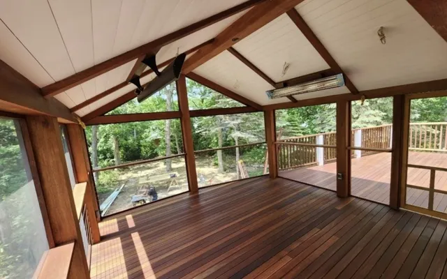 Inside a screened porch with a timber frame, hardwood floor and vaulted board ceiling