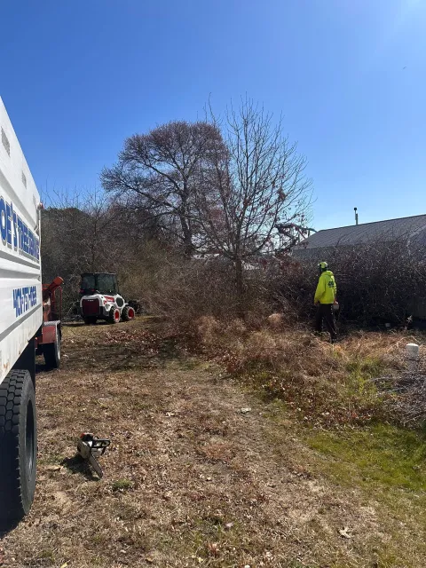 A man in a yellow vest is standing next to a truck in a field.