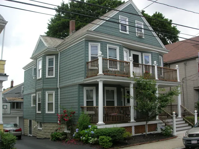 A green house with a porch and a car parked in front of it