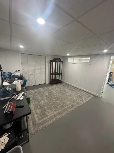 A living room in a basement with a rug and a hutch.
