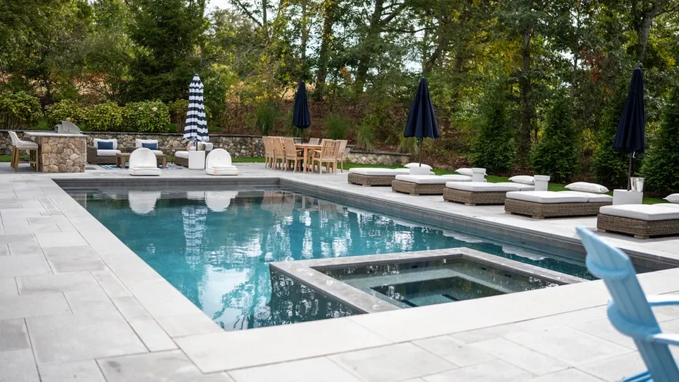 Modern swimming pool with integrated hot tub, lounge chairs, and dining area.