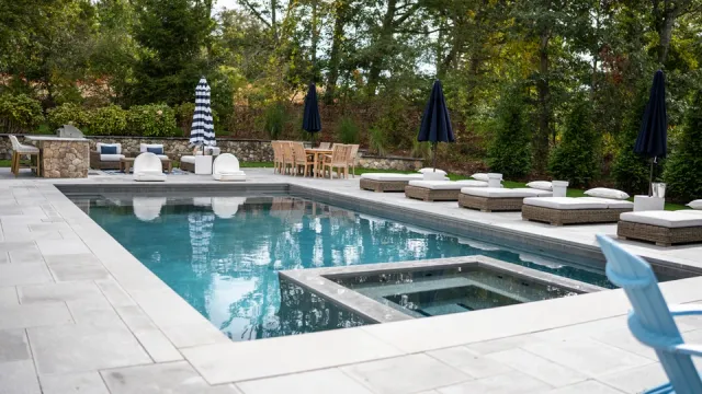 Modern swimming pool with integrated hot tub, lounge chairs, and dining area.