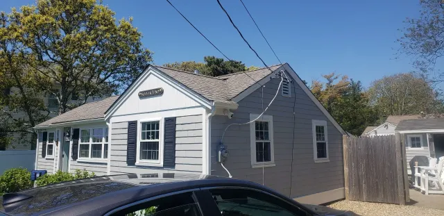 White house with black shutters and a small side addition, viewed from the street on a sunny day.