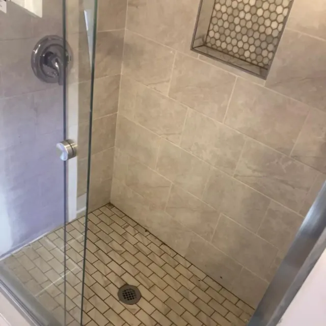 Walk-in shower with travertine tile walls and brick pattern floor by Link Services Pro in Holden, MA