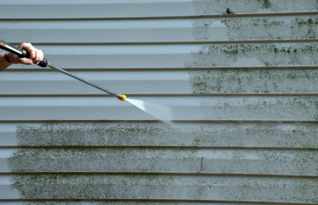 Pressure washer wand cleaning green algae off house siding