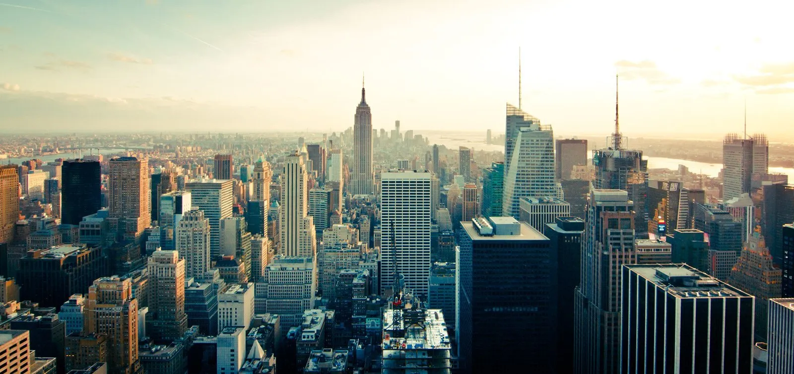 Aerial view of New York City skyline at sunset, with skyscrapers and a bright sky.