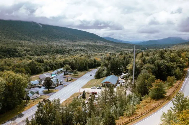 Aerial view of a rural property with buildings, a pool, and roads surrounded by forested mountains.