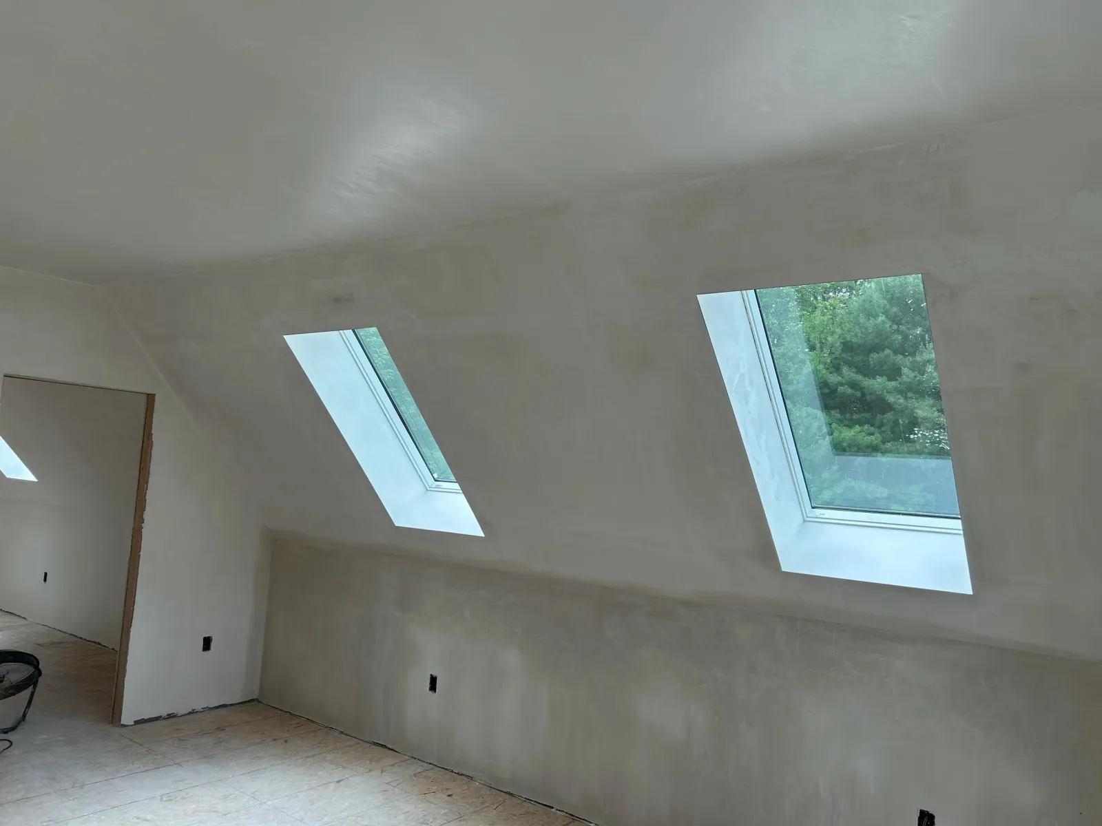 Interior of a room under construction with two skylights on a sloped ceiling and unfinished walls and floor.