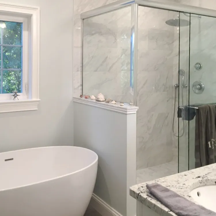 Modern bathroom with white marble tiles, a glass shower, and a freestanding white bathtub.