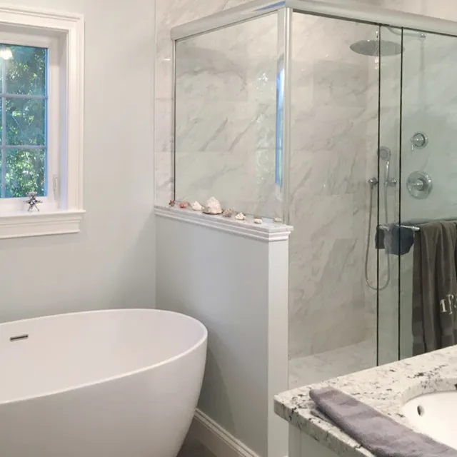Modern bathroom with white marble tiles, a glass shower, and a freestanding white bathtub.