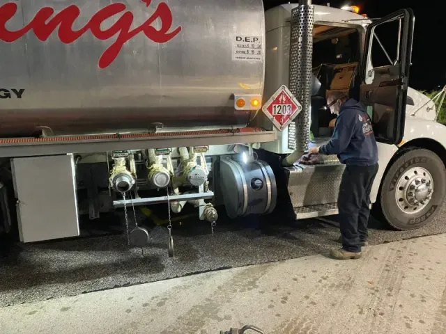 Truck driver inspecting a fuel tanker at night on a road shoulder