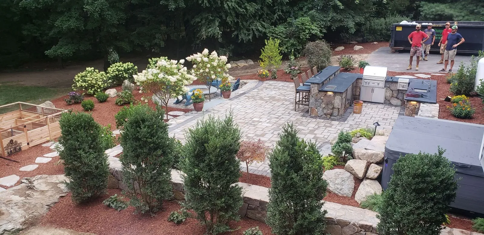 Terraced garden with shrubs, flowers, stone path, and people working in the background