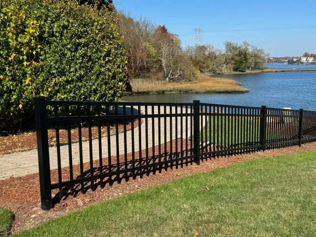A black fence surrounds a grassy area next to a lake.