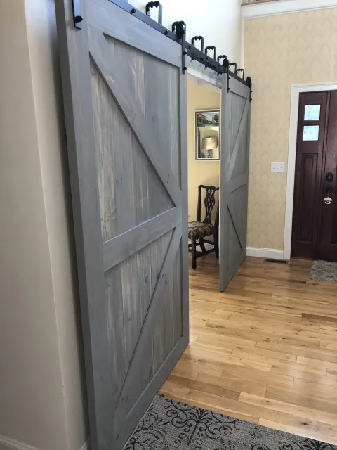 Sliding barn door with a wood finish on a black metal track, partially open, revealing a dining area with a chair and wall art.