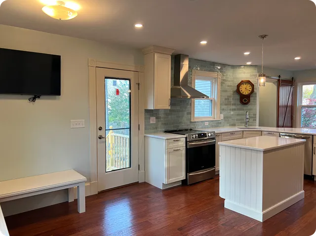 Kitchen with white cabinets, blue glass tile backsplash, island, and stainless range hood.