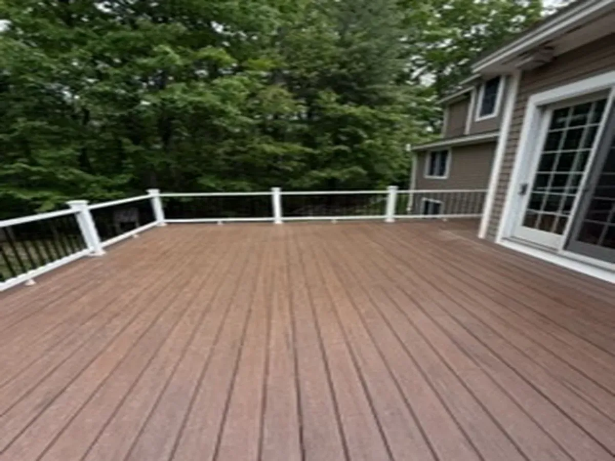 Large wooden deck with white railing beside a house and trees