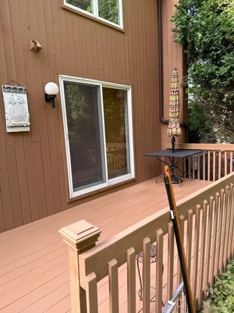 Wooden deck with patio furniture, umbrella, sliding glass door, outdoor lighting, and plants along the deck railing.