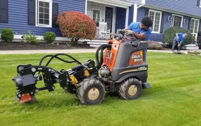 A man is driving a tractor on a lush green lawn in front of a house.