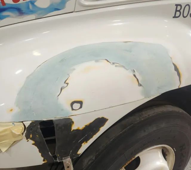 White car fender undergoing bodywork repair, with primer and putty applied.