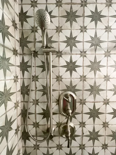 Close-up of a showerhead and faucet mounted on a wall with geometric patterned tiles.