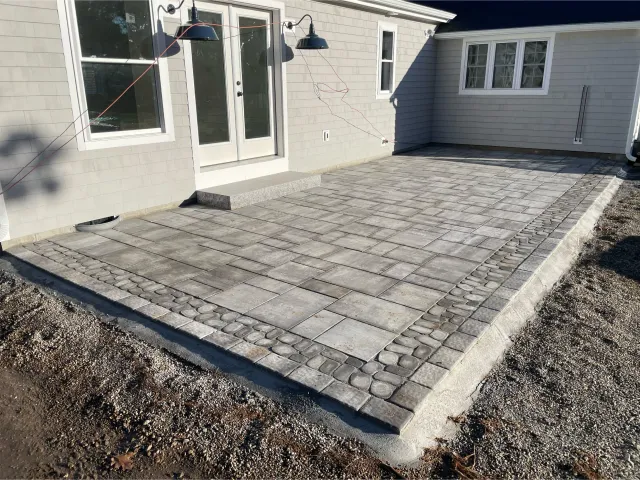 A gray limestone and river rock patio with a granite step built by The Englishmen Masonry