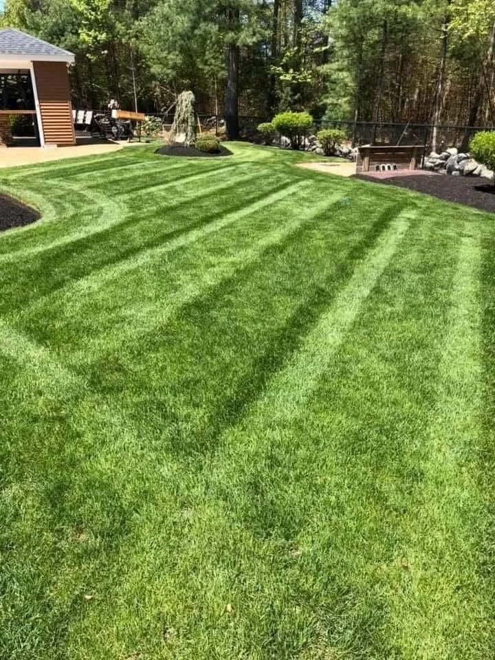 A person on a yellow riding lawnmower cuts green grass in front of a white barn-style building.
