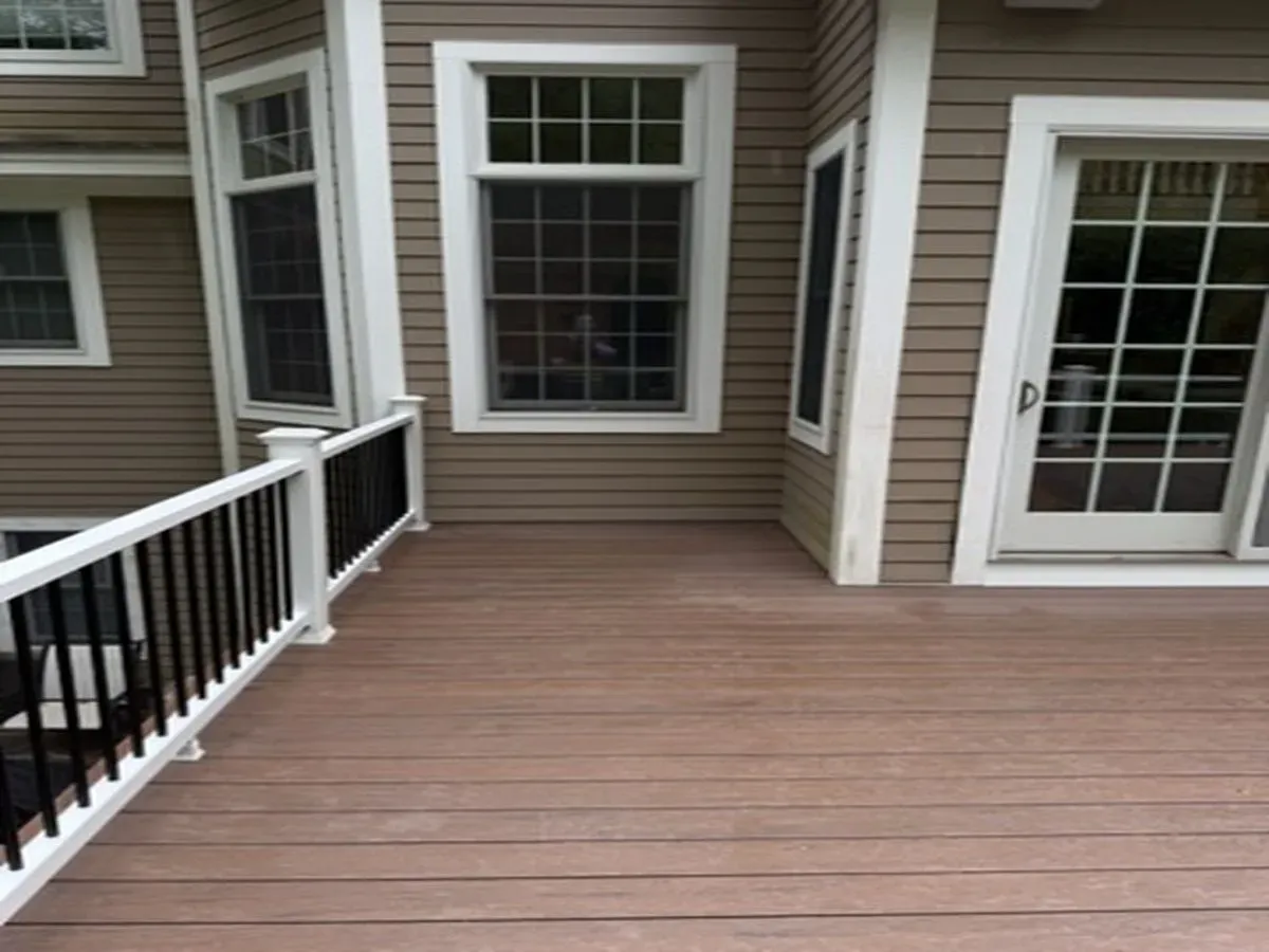 Wooden deck with white railing beside beige house exterior and sliding glass doors