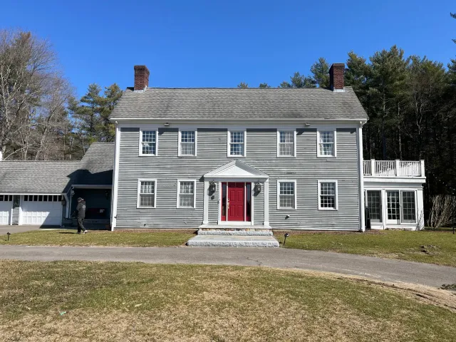 A large gray house with a red front door, multiple windows, and a small front porch set against a backdrop of trees. It looks stunning.