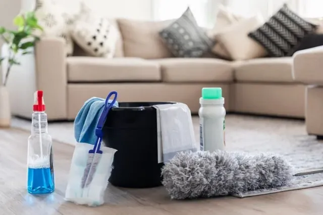 Cleaning supplies on a wooden floor in front of a beige sofa with pillows.