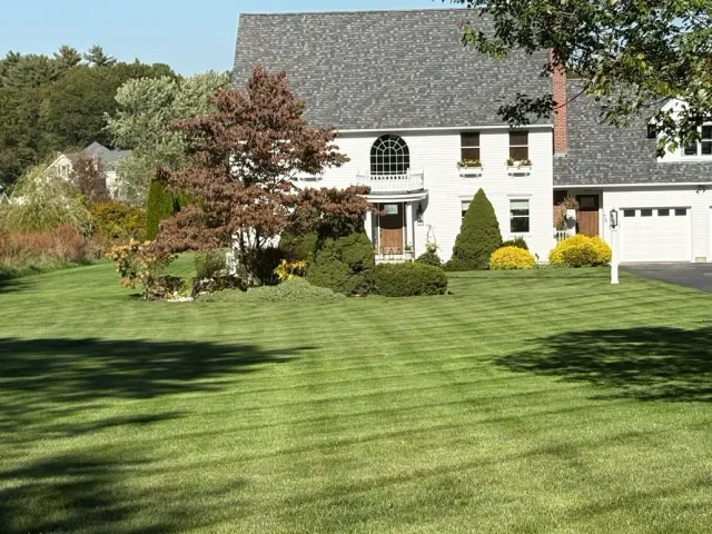 Suburban two-story house with white siding, a green lawn, trees, and a garage on the right.
