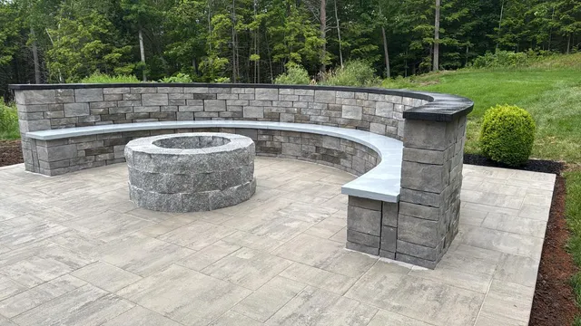 Circular stone fire pit with curved seating wall on a paved backyard patio