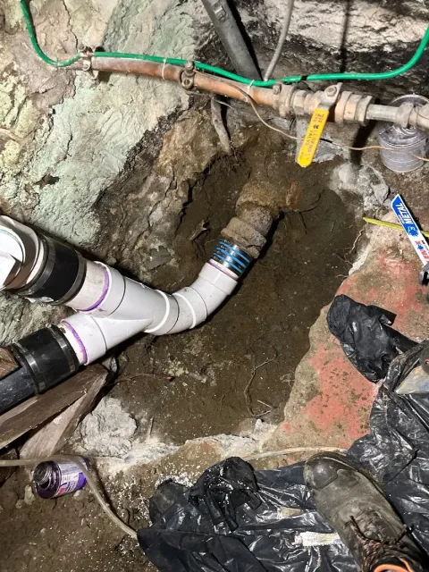 Underground plumbing pipe installation with construction tools and debris.