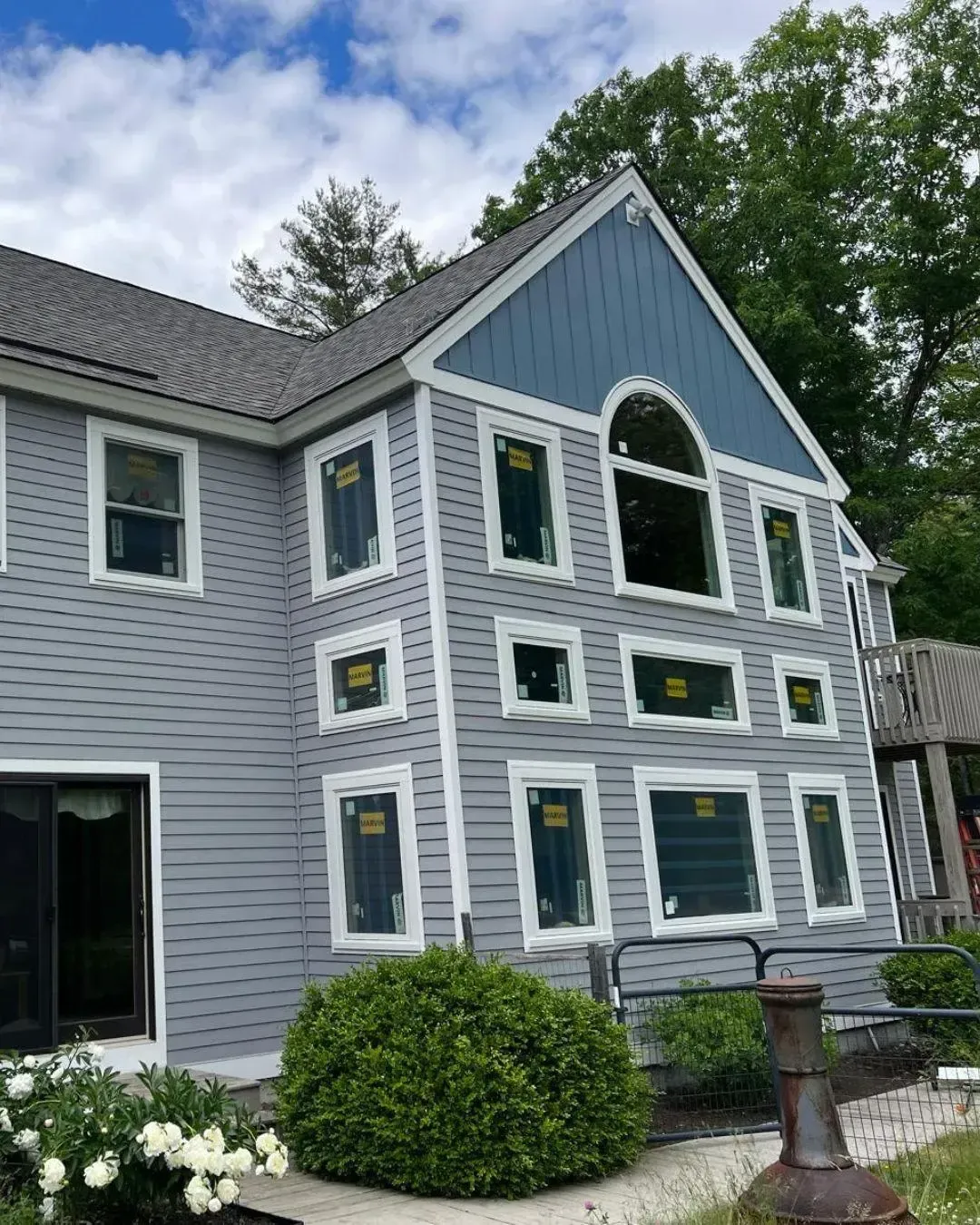 Full-house Marvin window replacement on a blue-grey clapboard home with a board-and-batten gable and an arched window, by Maia Construction