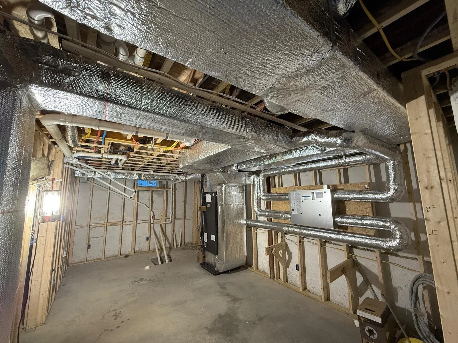 Construction site with exposed wooden framing and ductwork, including metal pipes, insulation, and electrical wiring.