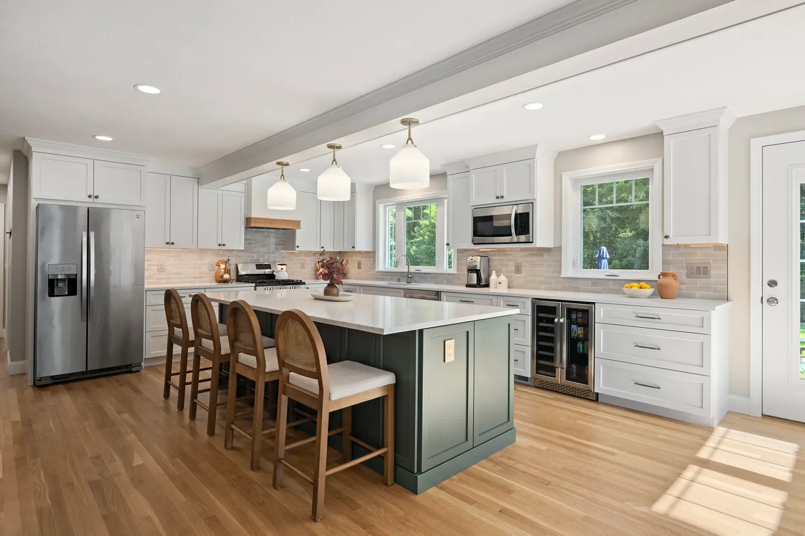 Bright renovated kitchen with green island, white cabinetry, pendant lights, and hardwood floors