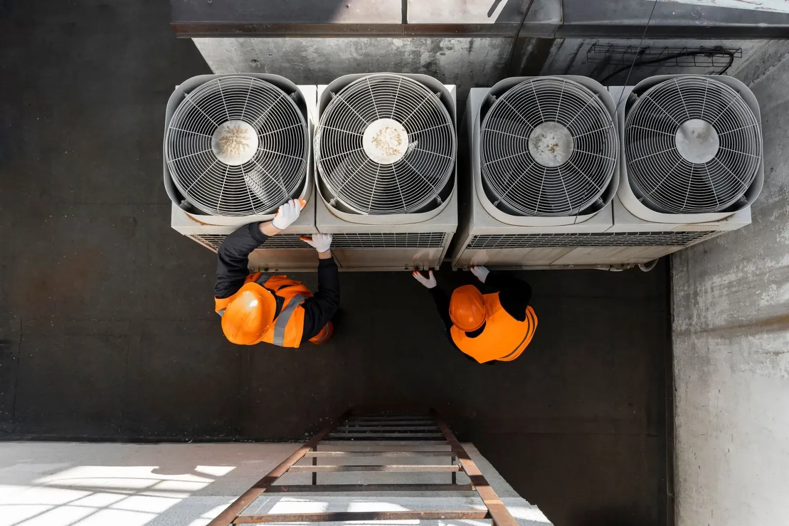 Two technicians in hard hats servicing rooftop condenser fans