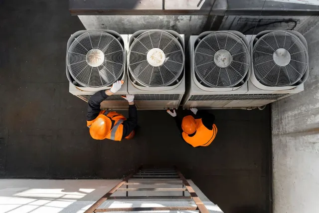 Two technicians in hard hats servicing rooftop condenser fans